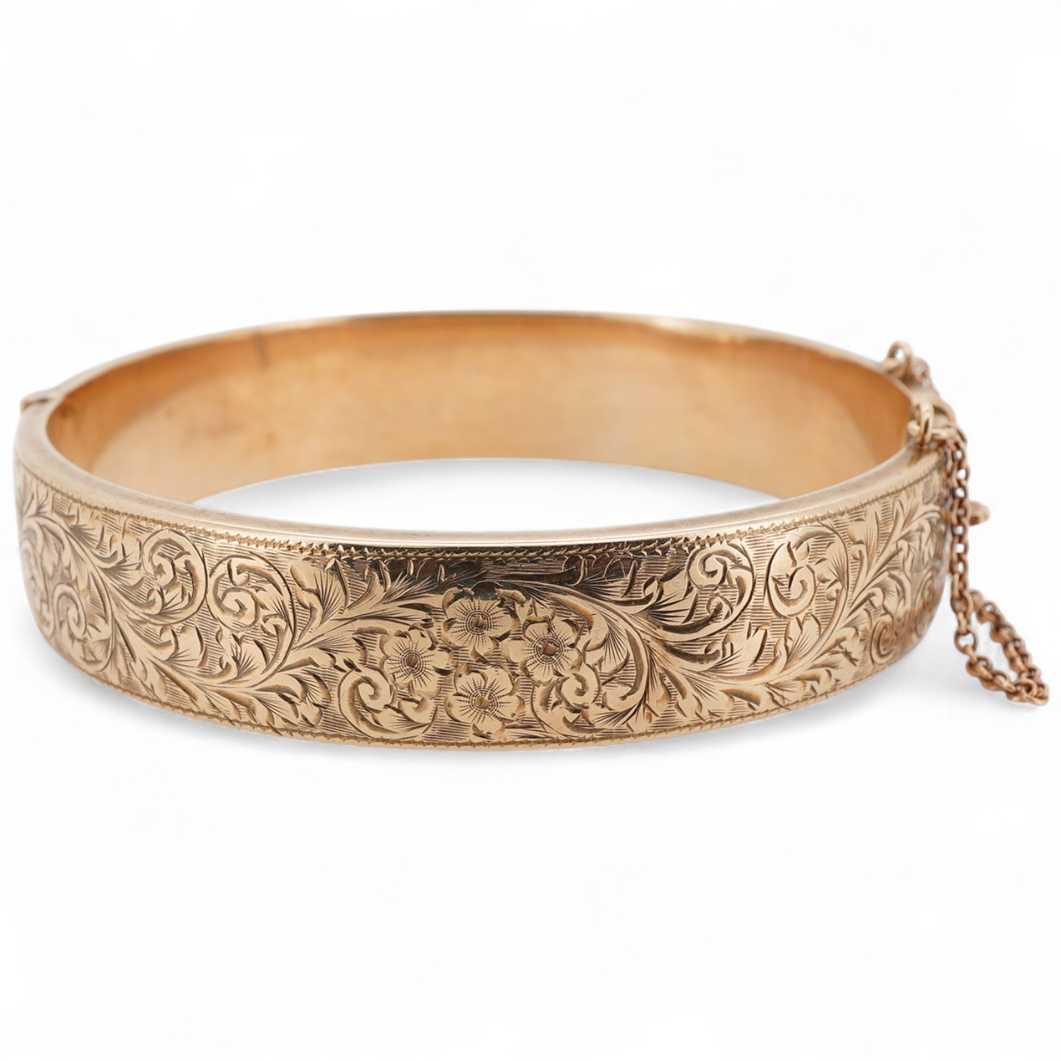 A 9ct gold bangle, of hinged construction, the front engraved with floral scrollwork, inner circumference approximately 17.7cm, British hallmarks, gross weight approximately 16 grams